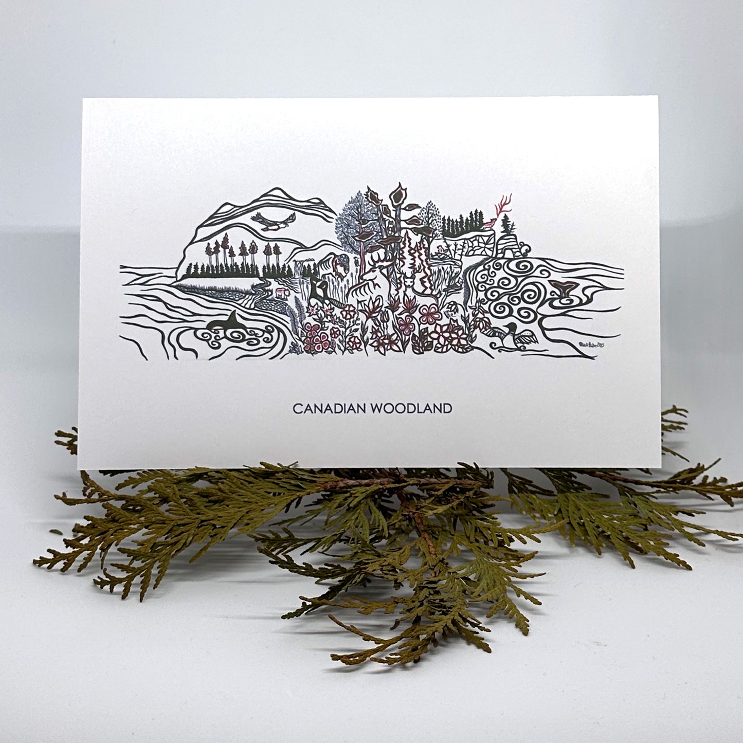 A greeting card with Patrick Hunter's Canadian Woodland work in woodland art style rests on cedar boughs.