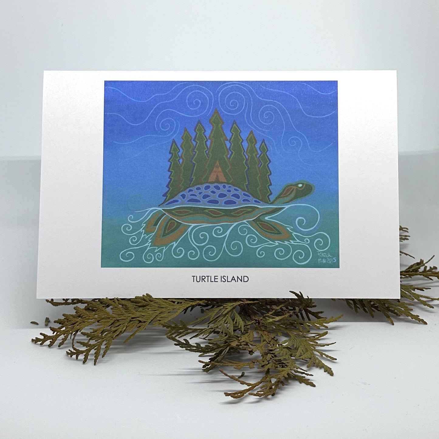 Patrick's painting of Turtle Island in woodland art style as a greeting card standing open on cedar boughs.